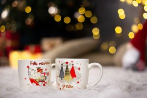 Two mugs with Christmas theme prints on a fluffy blanket with a blurry background and bokeh lights